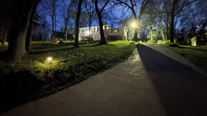 Una calle residencial nocturna con casas, árboles y una acera.