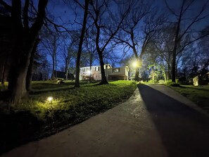 A residential street at night with houses, trees, and a sidewalk.