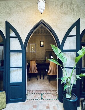 Un arco de entrada conduce a una habitación con un piano, sillas y una planta en maceta.