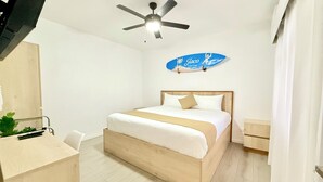 Et soveværelse med en seng, ventilator, opsat skilt, skrivebord og en plante.