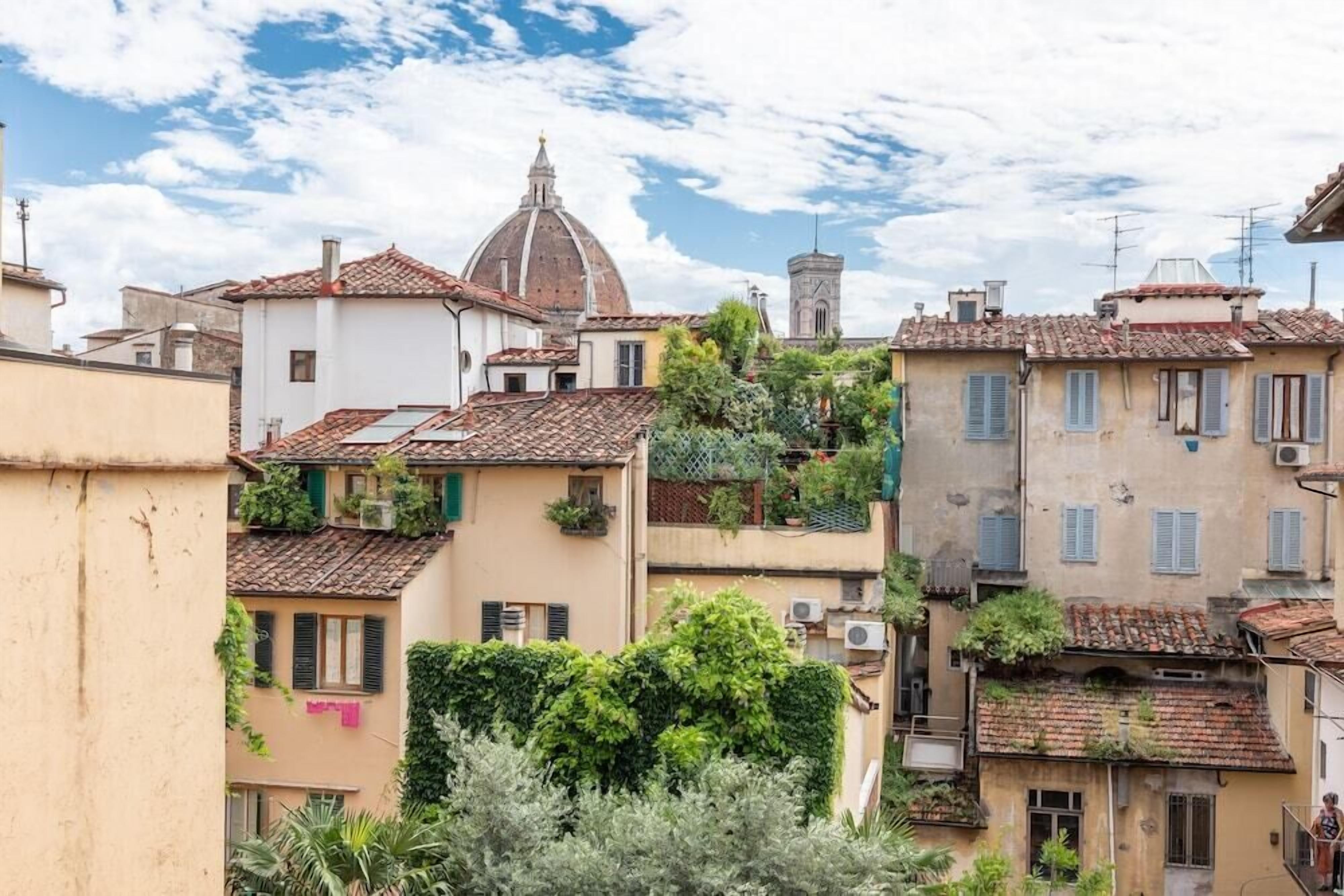 A historic town with terracotta-roofed buildings, a prominent dome, and lush greenery.
