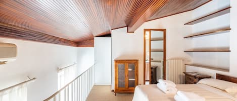 A hotel room with a wooden ceiling, a large bed, a wardrobe, and a mirror.