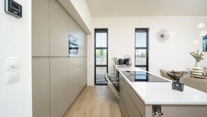 A modern kitchen with a central island, built-in appliances, and a dining area with a view. - Luxury 4 Guests Villa With Sunny Garden (Workum)