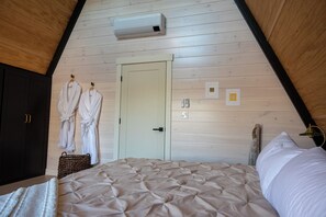 A bedroom with a sloped ceiling, a bed, a wardrobe, and a door. - Granite Meadows: Modern A-Frame with Hot Tub (Thomaston)