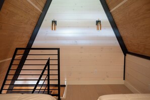 A sloped ceiling with wooden paneling, a metal ladder, and two wall-mounted light fixtures.