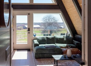 A room with a green sofa, a small table, and a view of a fenced area with trees and buildings.