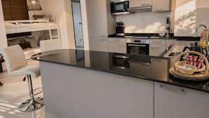 Ett modernt kök med en central köksö, inbyggda vitvaror och en matplats med barstolar.