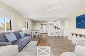 A modern living room with a grey sofa, a wooden coffee table, and a ceiling fan. - Windward Waves & Bayview Bliss | Pool + Renovated (Ocean City)