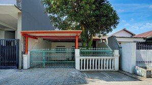 A gated residential area with a paved entrance, a covered porch, and a tree providing shade.