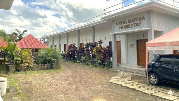 A building with a sign reading 'GRIYA MANISA HOMESTAY' and a covered area with a car parked outside.