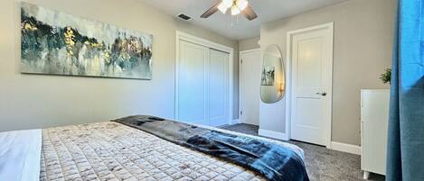 A bedroom with a bed, a ceiling fan, a painting, a wardrobe, and a mirror.