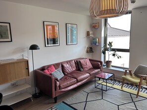 Ein modernes Wohnzimmer mit Ledersofa, Couchtisch, Stehlampe und einem großen Fenster mit Blick.