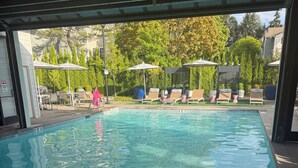 Piscina con sillas de descanso y sombrillas, rodeada de vegetación.
