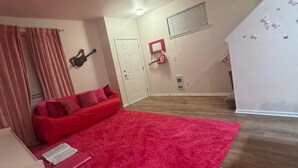 Una habitación con un sofá rojo, un tapete rosa, una mesita y una escalera.