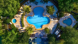 Vista aérea de un resort con una piscina central, varias piscinas más pequeñas y zonas de descanso alrededor.
