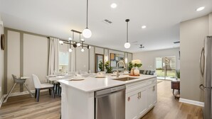 Una cocina moderna con una isla central, electrodomésticos de acero inoxidable, iluminación colgante y vistas al exterior.