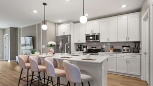 Una cocina moderna con armarios blancos, electrodomésticos de acero inoxidable y una isla central con taburetes de bar.
