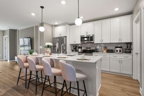 A modern kitchen with white cabinets, stainless steel appliances, and a central island with bar stools. - Stylish Home with Pool Hot Tub and Parking (Kissimmee)