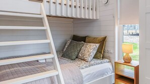 A bunk bed with a ladder, a bedside table with a lamp, and a window with a view of an outdoor area. - Villa orion 57 by Interhome (Kemiönsaari)