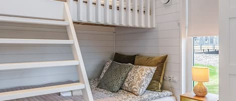 A bunk bed with a ladder, a bedside table with a lamp, and a window with a view of an outdoor area.