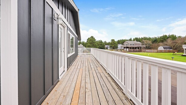 A wooden deck with a white railing, a gray building, and a clear blue sky. - Beautiful 4-bedroom house in enchanting Long Beach perfect for families (Long Beach)
