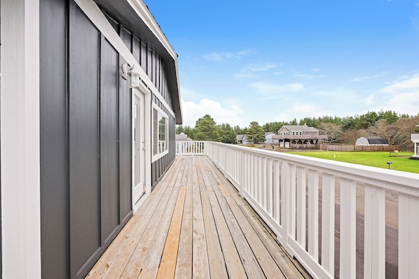 Une terrasse en bois avec une balustrade blanche, un bâtiment gris et un ciel bleu dégagé.