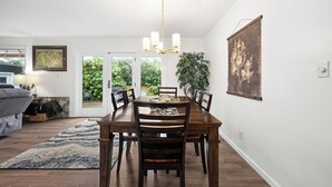 A dining area with a wooden table, chairs, a chandelier, a large plant, and a painting on the wall. - Beautiful 4-bedroom house in enchanting Long Beach perfect for families (Long Beach)