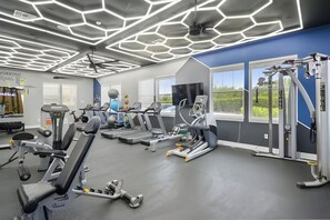 Ein Fitnessraum mit Trainingsgeräten, einem großen Fenster und einer Decke mit geometrischer Beleuchtung.