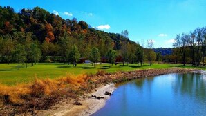 A serene lakeside setting with a grassy area, trees, and a small building.