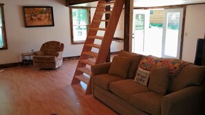 A living room with a wooden staircase, a sofa, a chair, and a framed picture on the wall.