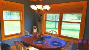A dining room with a wooden table, chairs, a chandelier, and large windows with a view of a grassy area.