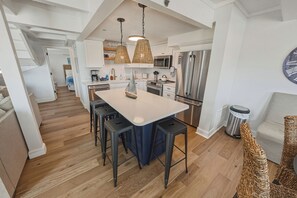 A modern kitchen with a central island, bar stools, and a stainless steel refrigerator. - OCEANFRONT 3-Bedroom in Duck: Beach + Pool + Walk to Shops (Duck)