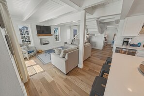 A spacious living area with a sofa, a television, and a staircase leading to another level. - OCEANFRONT 3-Bedroom in Duck: Beach + Pool + Walk to Shops (Duck)