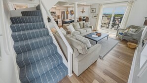 Un escalier recouvert d’une moquette à motifs, un ensemble de canapés avec des coussins, une table basse et une vue sur l’extérieur.