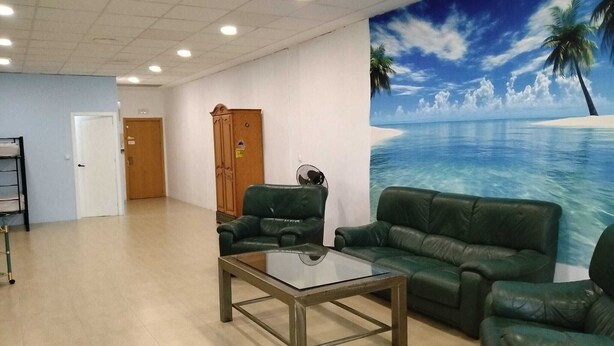 Un vestíbulo amplio con una mesa de centro de vidrio, sofás de cuero verde, un armario de madera y un mural con una escena de playa.