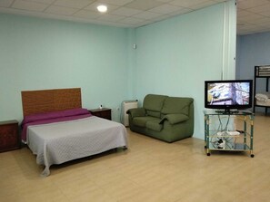 A bedroom with a bed, a green sofa, a TV on a stand, and a small table with a heater.