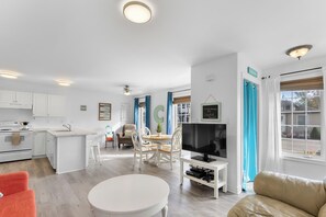 A modern kitchen with white cabinets, a dining area with a white table and chairs, a TV on a stand, and a living area with a sofa and a coffee table. - Lincoln Landing- Steps to the beach (Fort Erie)