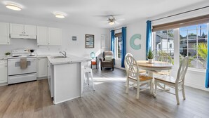Una cocina moderna con armarios blancos, una isla central y una zona de comedor con una mesa de madera y sillas blancas.