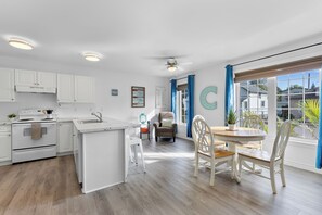 A modern kitchen with white cabinetry, a central island, and a dining area with a wooden table and white chairs. - Lincoln Landing- Steps to the beach (Fort Erie)