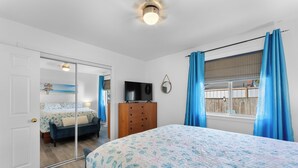 Un dormitorio con cama, cómoda, televisor, espejo y ventana con cortinas.