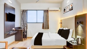 Quarto de hotel moderno com uma cama, escrivaninha, cadeira, televisão e janela com cortinas.