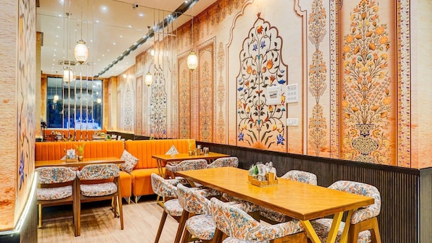 Um restaurante com mesas e cadeiras de madeira, área de bar e decoração de parede elaborada.