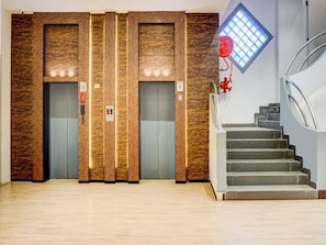 A modern elevator with wood paneling, a red emergency pull cord, and a stairwell with a glass window. - Super Townhouse Bombay Exhibition Centre (Mumbai)