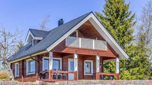A two-story house with a covered porch, a chimney, and a stone retaining wall.