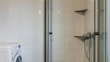 A bathroom with a glass-enclosed shower, a washing machine, and tiled walls.