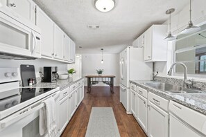 A modern kitchen with white cabinets, a central island, and a stainless steel sink. - 3BR Pool Putting Green | Good Morning Rentals (Jacksonville Beach)