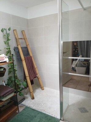 A bathroom with a shower, a towel rack with a towel, a plant, and a shelf with folded towels. - Le cocon provençal, gîte with private jacuzzi (Vers-Pont-du-Gard)