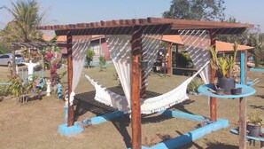 A hammock under a wooden pergola with blue accents, surrounded by potted plants and a clear sky. - Chalet São Jorge where nature predominates (São Pedro)