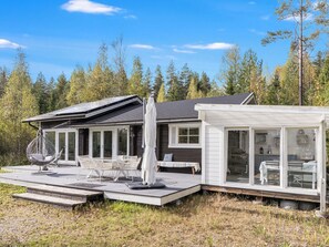 A modern cabin with a deck, outdoor seating, and a glass-enclosed room. - Teurajärven helmi by Interhome (Tammela)
