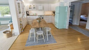 Una cocina compacta con armarios blancos, una mesa de comedor de madera y un refrigerador verde azulado.